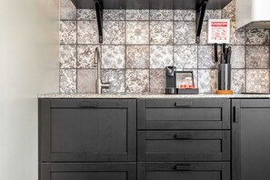 Una cocina con salpicadero de azulejos, una cafetera y un juego de cuchillos.