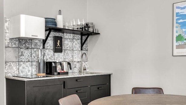 Una cocina moderna con estufa integrada, cafetera y repisa colgante con vajilla.