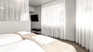 Habitación de hotel con cama, televisor montado en la pared y cortinas traslúcidas.