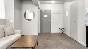 Una sala moderna con un sofá, una mesa de centro de madera, un espejo redondo y una puerta gris.