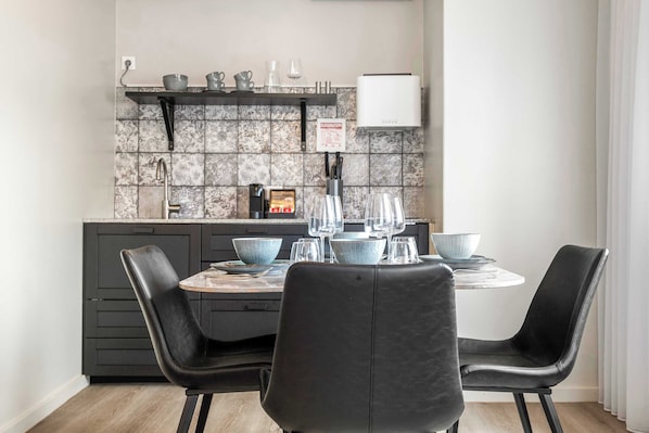A modern kitchen with a dining table set for four, black chairs, and a tiled backsplash.
