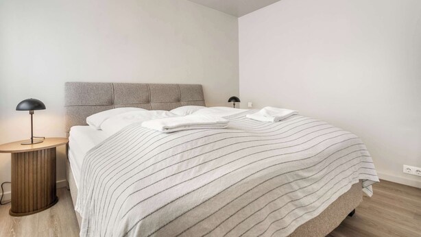A bedroom with a bed, a nightstand, a lamp, and a wall socket. - Swan Superior Studio (Reykjavík)