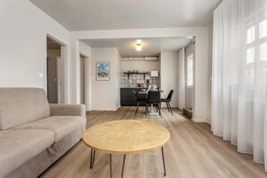 A modern living room with a sofa, a round wooden coffee table, and a dining area with chairs and a table.