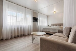 A modern, well-lit room with a bed, a sofa, a round table, and a TV mounted on the wall.