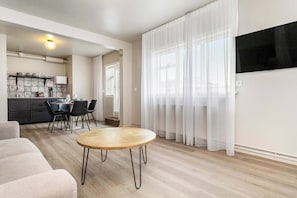 A modern living room with a round wooden table, a sofa, and a kitchen area with a dining set.