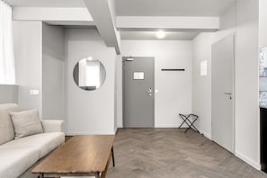 A modern living room with a sofa, a wooden coffee table, a round mirror, and a grey door.