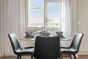 A dining area with a table set for two, two black leather chairs, and a window with white curtains. - Swan Superior Studio (Reykjavík)