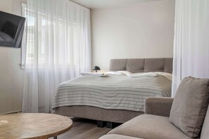 Une chambre d’hôtel avec un lit, un téléviseur fixé au mur, une table ronde en bois et un canapé.