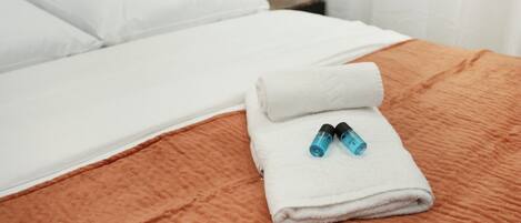 Cama bem arrumada com uma toalha branca dobrada e dois frascos azuis.