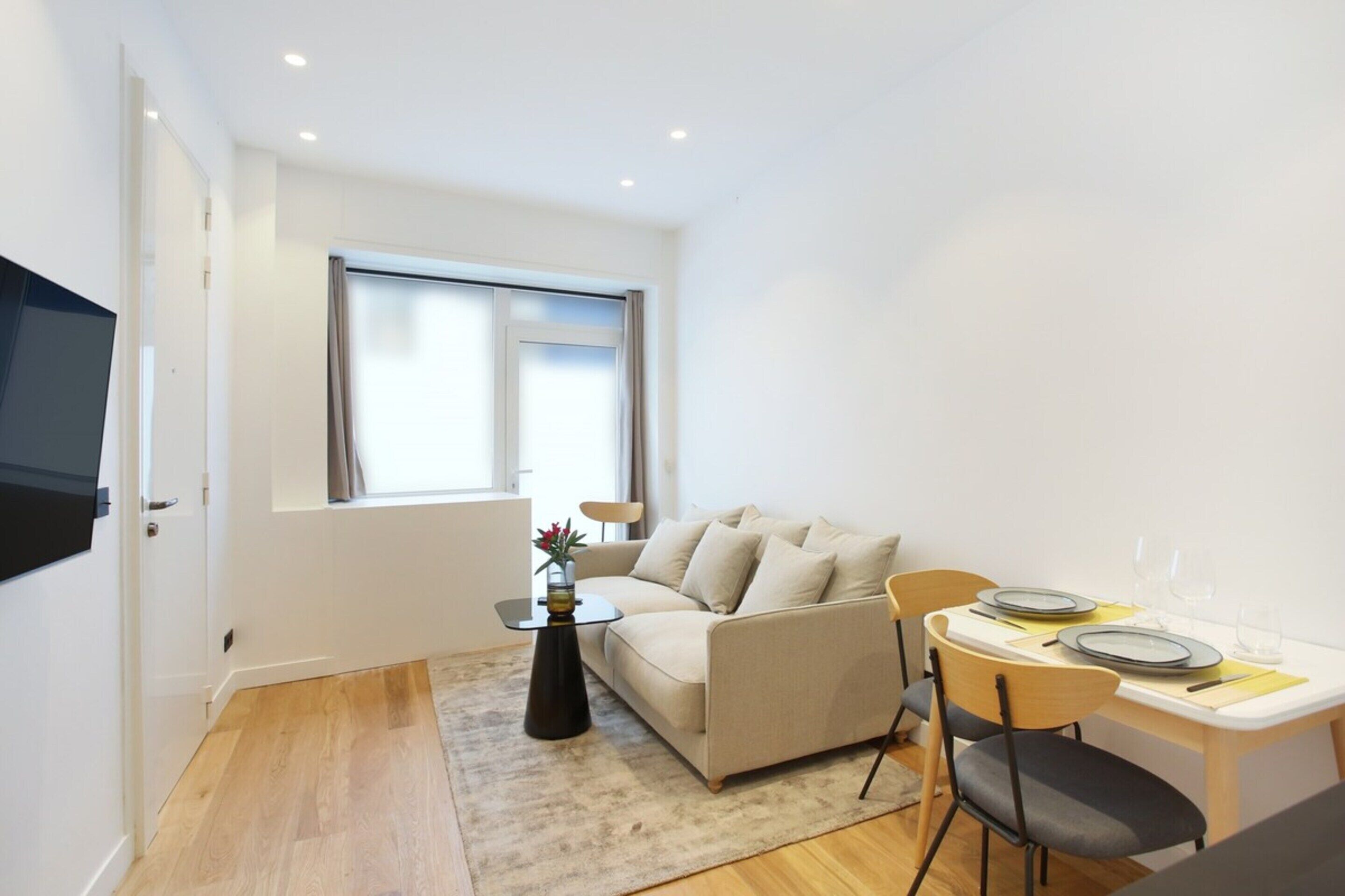 Un espacio habitable compacto con un sofá, una mesa de comedor para dos personas y una mesita auxiliar con un jarrón.