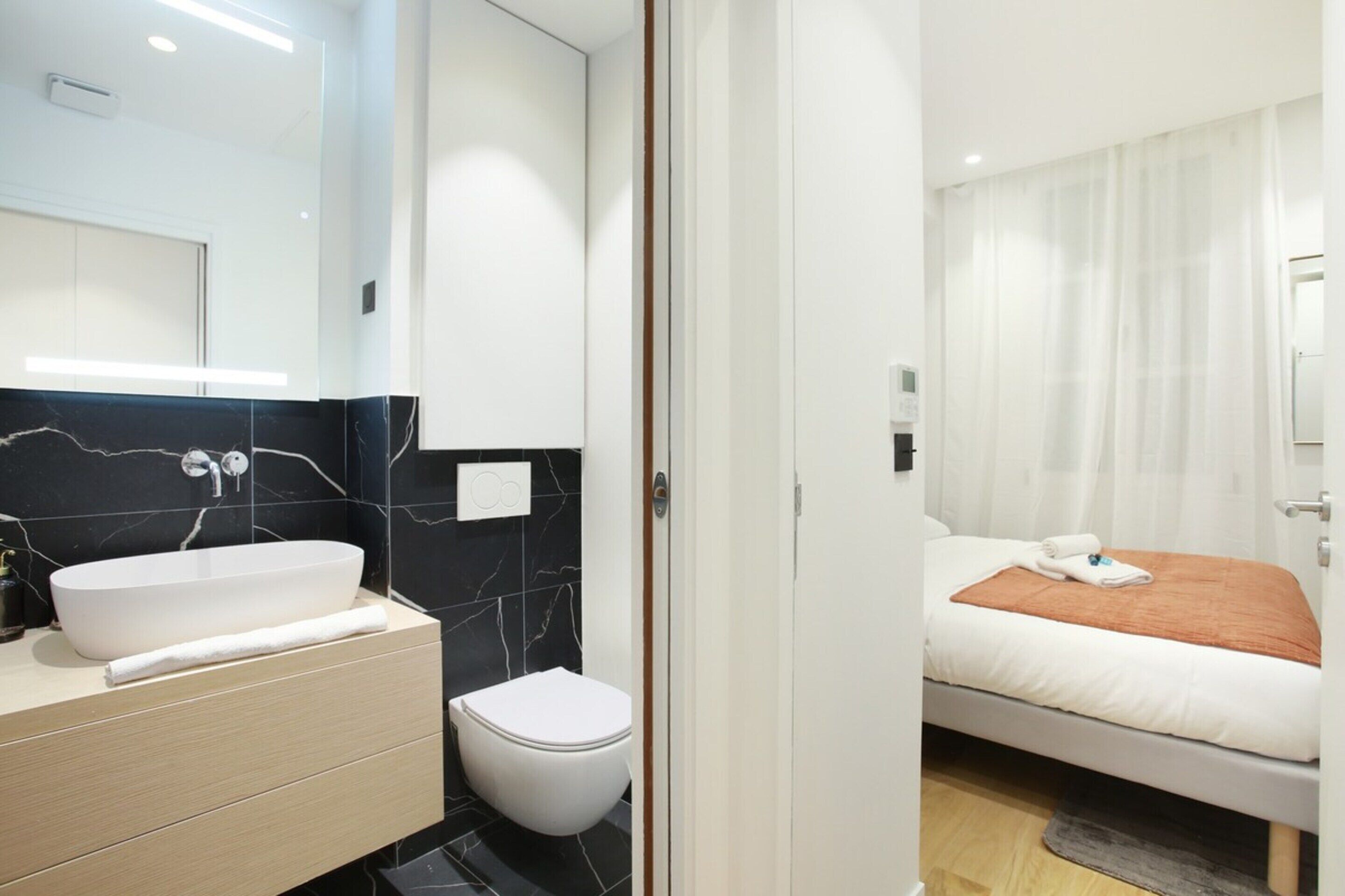 Un baño moderno con lavamanos blanco, salpicadero de mármol y retrete.