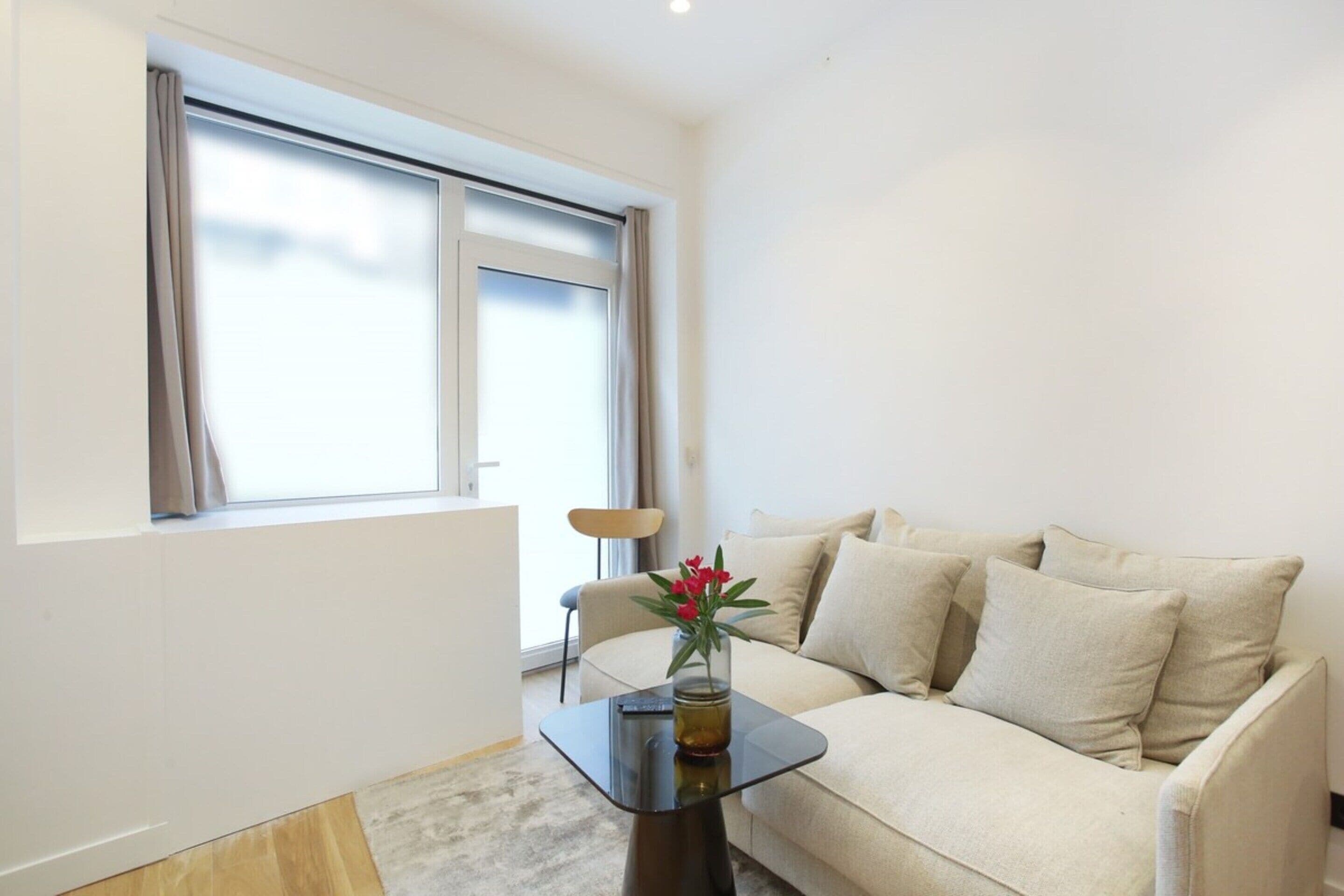 Een moderne woonkamer met een bank, een glazen salontafel en een vaas met bloemen.