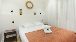 Ένα υπνοδωμάτιο με ένα κρεβάτι, ένα κομοδίνο, έναν καθρέφτη και ένα παράθυρο με κουρτίνες.