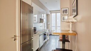 A modern kitchen with stainless steel appliances, a dining area with a table and chairs, and a view of the outside through a large window.