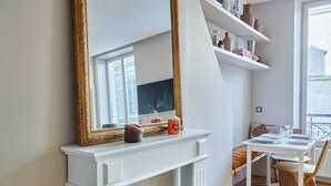 A room with a white fireplace, a large ornate mirror, a dining table set for two, and a window with blinds. - Superb Apartment Avenue Montaigne/saint Honore (Paris)