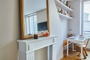 Ein Zimmer mit einem weißen Kamin, einem großen, verzierten Spiegel, einem für zwei Personen gedeckten Esstisch und einem Fenster mit Jalousien.