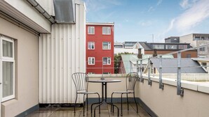 A small outdoor patio with a table and two chairs, a metal railing, and a view of a red building in the background.