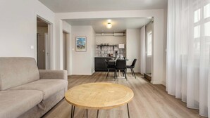 A modern living room with a sofa, a round wooden coffee table, and a dining area with chairs and a table.