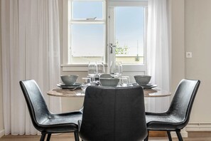 Comedor con una mesa dispuesta para dos, dos sillas de cuero negro y una ventana con cortinas blancas.