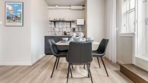 A modern dining area with a round table, black chairs, and a kitchen in the background.