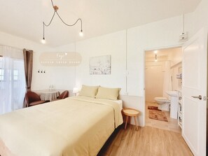 A hotel room with a bed, bedside table, and a small round table with chairs. There is a bathroom visible through an open door. - Little Latte House (Chalong)