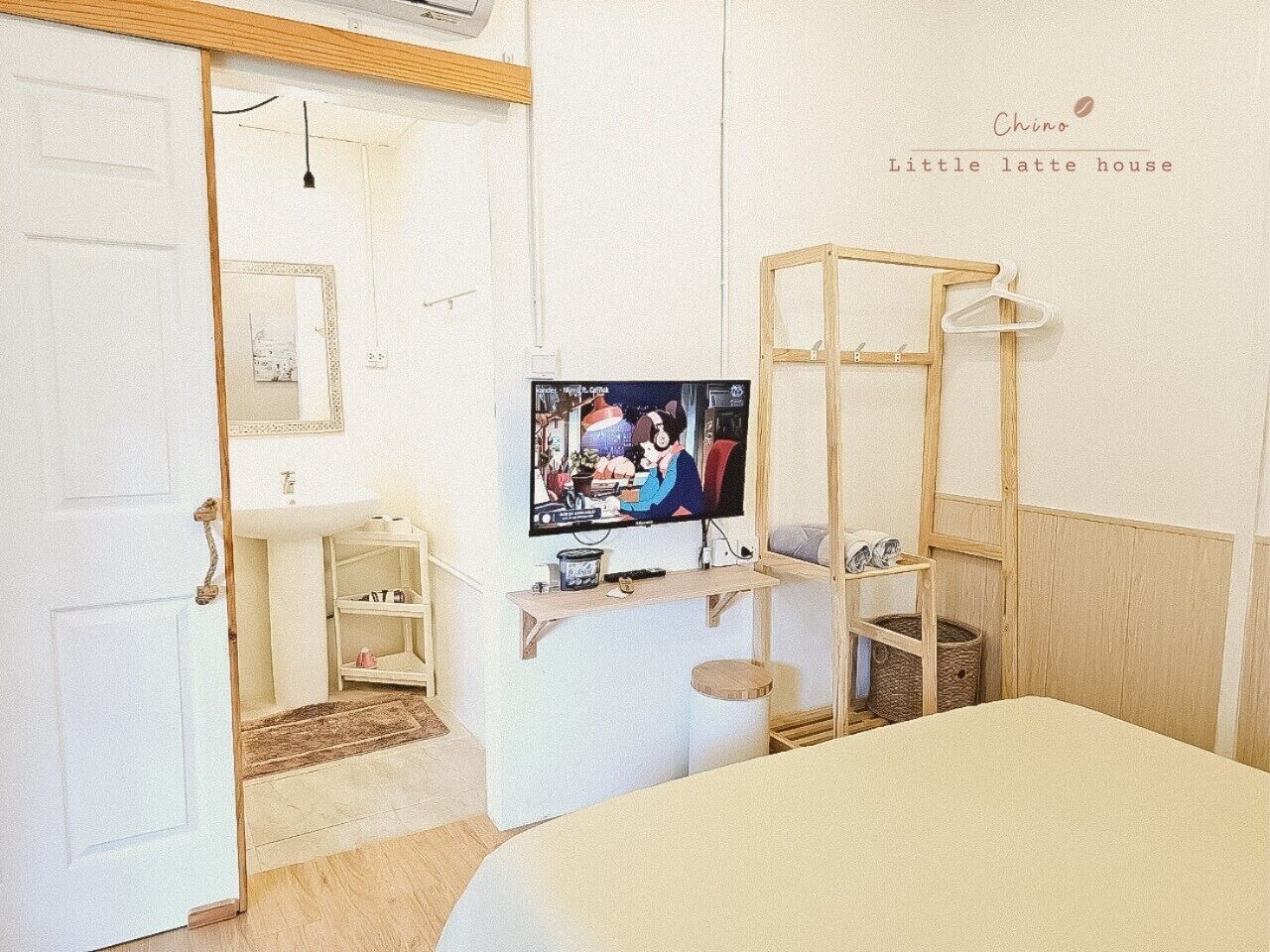 Een knus kamertje met een bed, een televisie, een houten plank en een kledingrek.