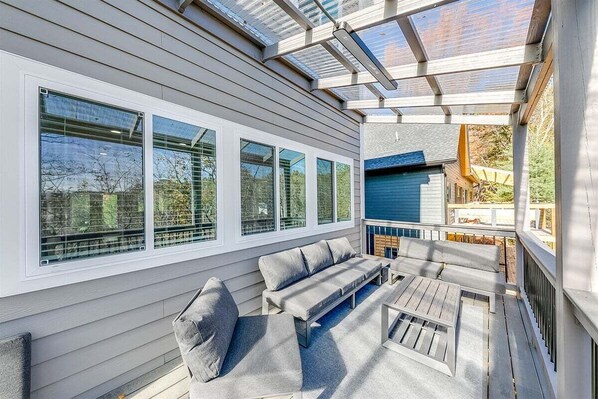 A covered outdoor seating area with a sofa and table, large windows, and a blue building in the background. - Jack–Modern 4-Level Luxury Retreat in Innsbruck (Helen)