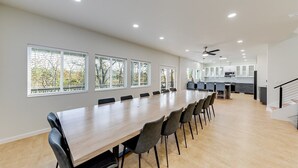 A spacious dining area with a long table and chairs, a kitchen in the background, and large windows with blinds. - Jack–Modern 4-Level Luxury Retreat in Innsbruck (Helen)