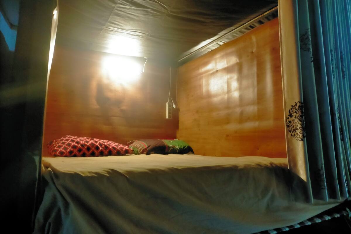 A single bed with a patterned pillow, a blanket, and a wall-mounted light fixture.