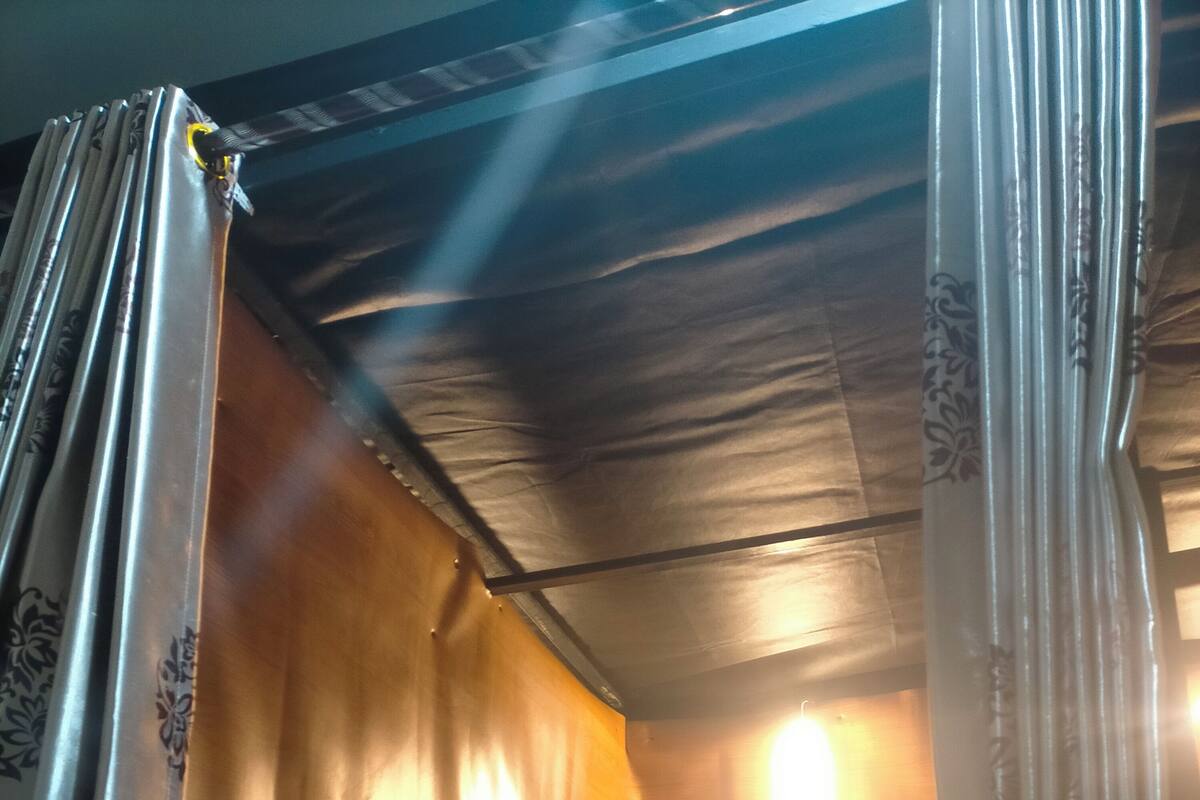 A single bed with a green mattress and a yellow pillow in a room with wooden walls and a slanted ceiling.