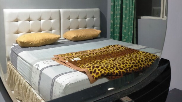Un letto con testiera imbottita, due cuscini, una coperta fantasia e un comodino con un telecomando.