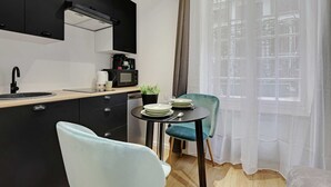 A modern kitchen with black cabinets, a black countertop, a coffee machine, and a small table with chairs.
