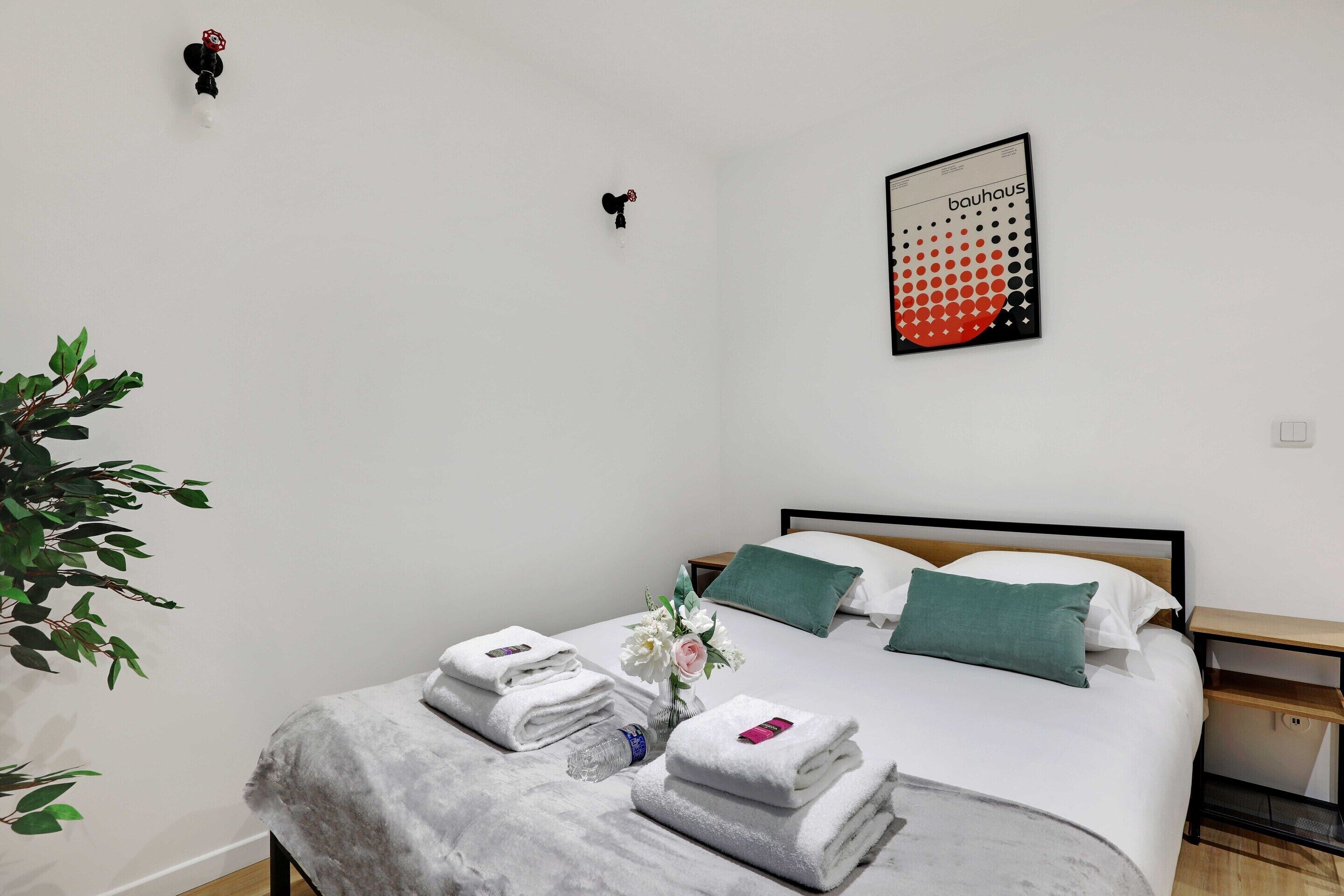 A neatly made bed with white linens, a green pillow, and a vase with flowers.