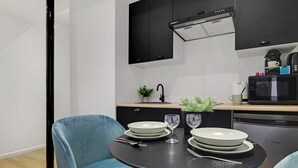 A modern kitchen with black cabinets, a black countertop, and a dining area with two blue chairs and a round table set with plates and glasses.