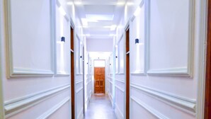 A long, narrow hallway with wooden flooring and white walls with paneling. - DOM PRECIOUS LODGE (Dodoma)
