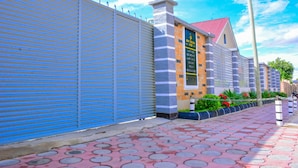 A building with a closed blue shutter, a brick facade, and a red roof. - DOM PRECIOUS LODGE (Dodoma)