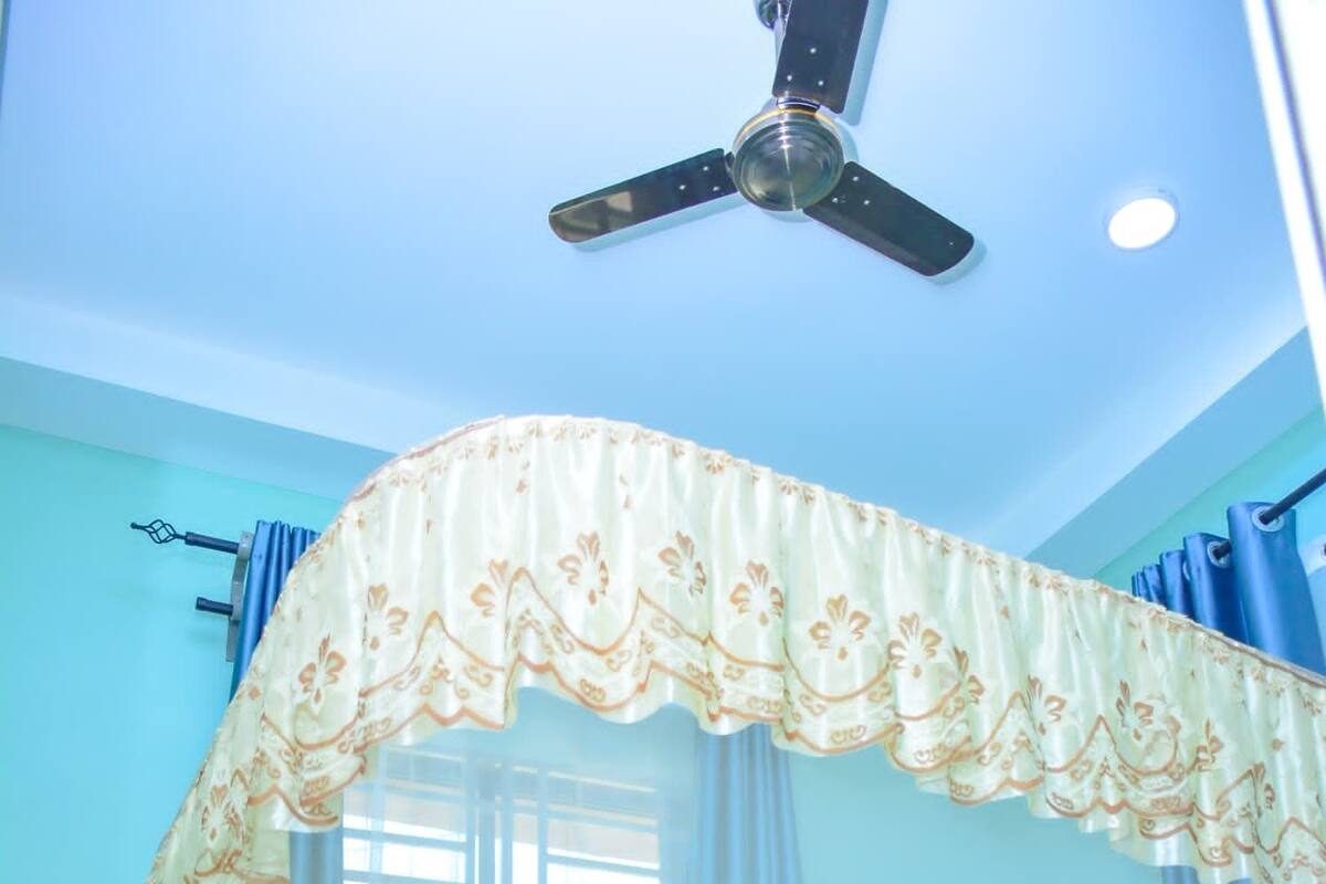 A room with a bed, a ceiling fan, and curtains.