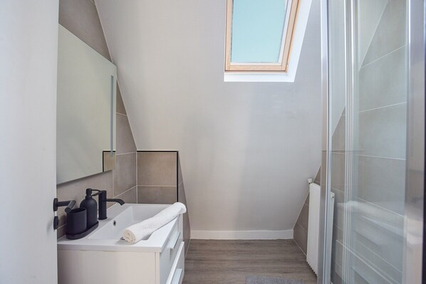 Une salle de bain moderne avec une lucarne, un lavabo blanc et un porte-serviettes.