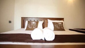 A neatly made bed with two pillows featuring elephant designs, a brown blanket, and a pair of rolled towels on the bed. - Harambathenna Resort Anuradhapura (Anuradhapura)