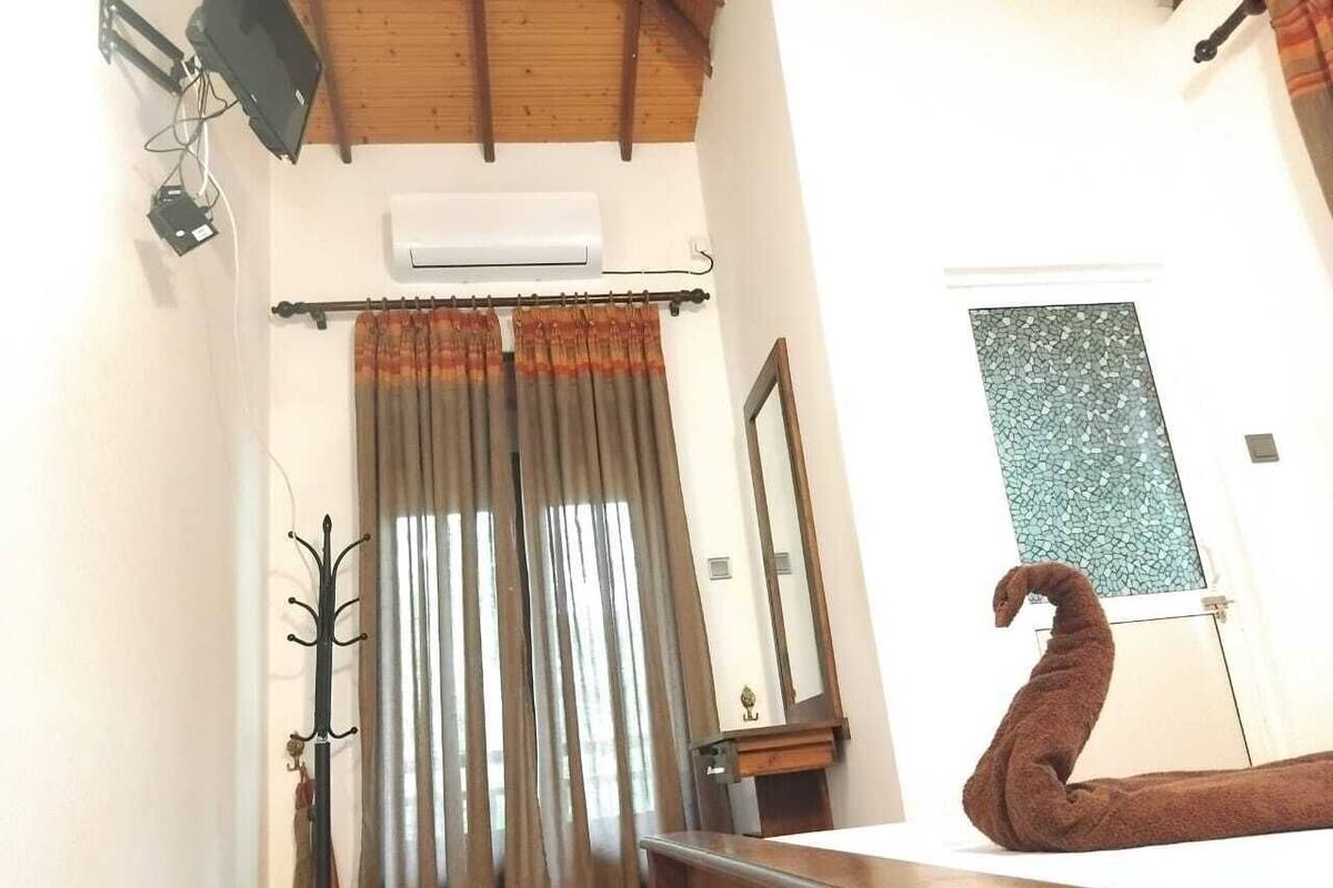 A bedroom with a wooden bed, a mirror, a window with a mosaic design, and an air conditioning unit.