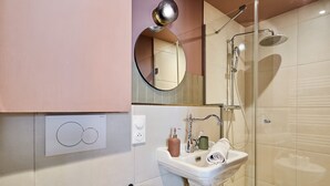 A modern bathroom with a glass-enclosed shower, a sink with a mirror above it, and a toilet paper holder on the wall. - Charming Studio Center of Paris (Paris)