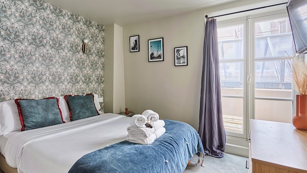 A bedroom with a bed, a nightstand, and a window with a view of buildings. - Charming Studio Center of Paris (Paris)