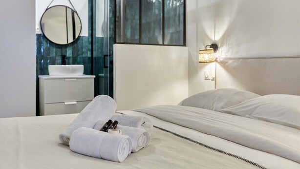 A modern hotel room with a neatly made bed, a round mirror, a white sink, and a wall-mounted light fixture. - Superb Apartment Arc de Triomphe (Paris)
