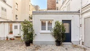 A courtyard with a small building featuring a window and a door, surrounded by potted plants and cobblestone flooring. - Superb Apartment Arc de Triomphe (Paris)