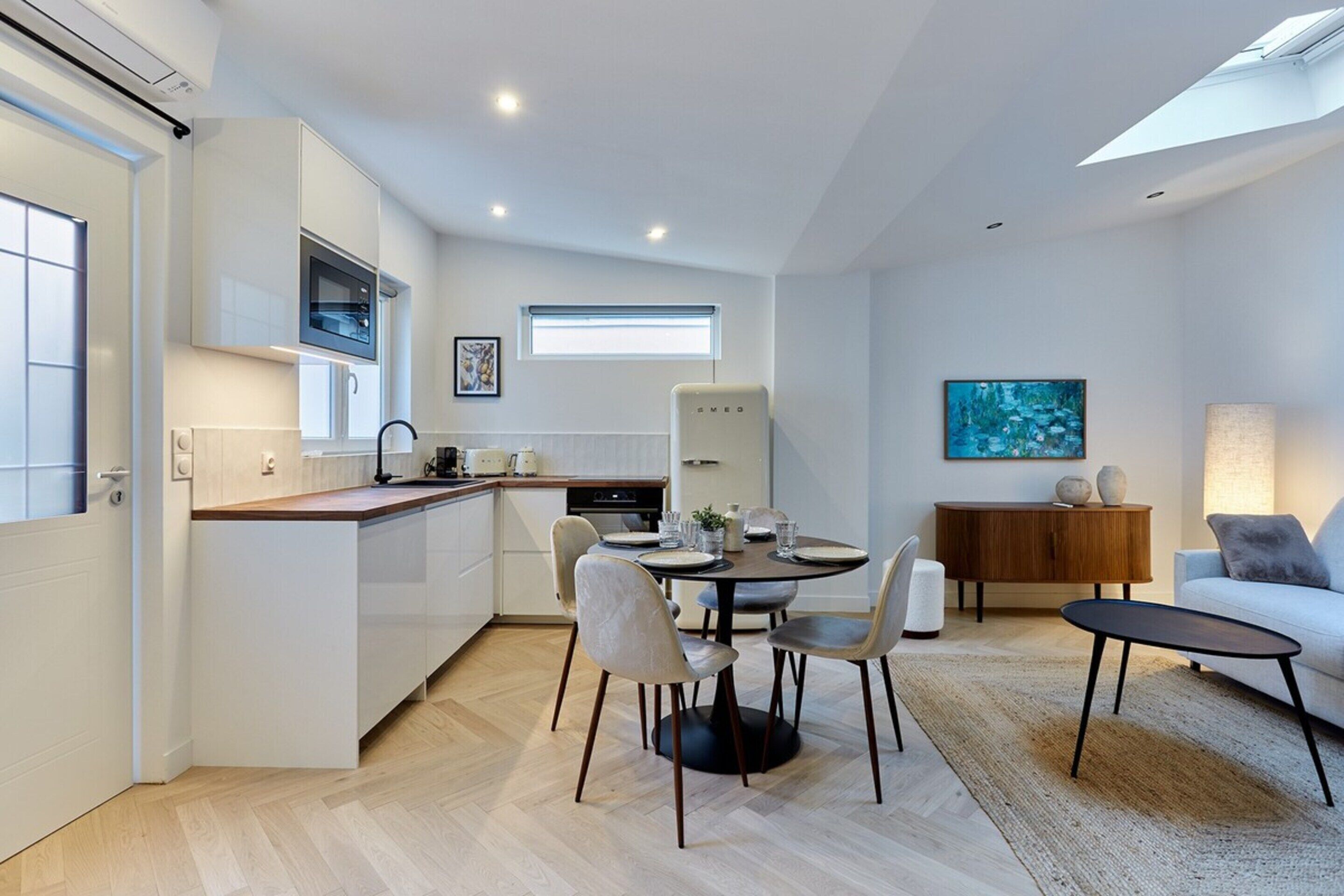 A modern kitchen with white cabinetry, a dining area with a round table and chairs, a sofa, and a lamp.