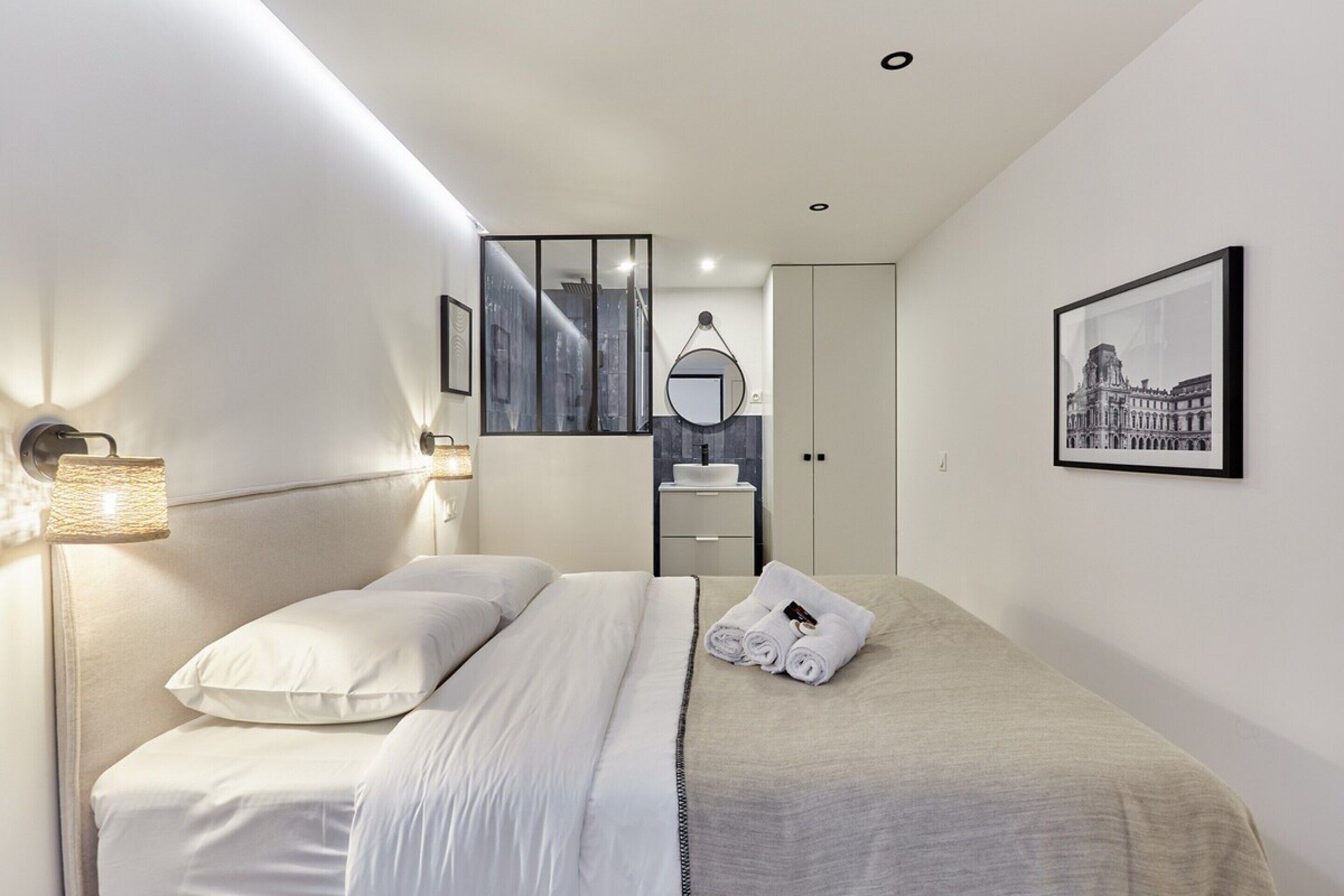 A modern bedroom with a bed, a bedside table, a mirror, and a framed picture on the wall.