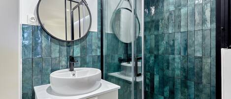 A bathroom with a round mirror, white sink, and glass shower enclosure.