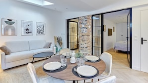 A modern living room with a sofa, dining table set for four, and a staircase leading to another room. - Superb Apartment Arc de Triomphe (Paris)