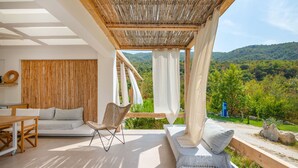 A modern outdoor living space with a sofa, chair, and dining table, overlooking a lush green landscape. - Aristi Villa Dio in Olimpiada (Aristotelis)