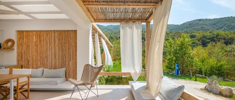 A modern outdoor living space with a sofa, chair, and dining table, overlooking a lush green landscape.